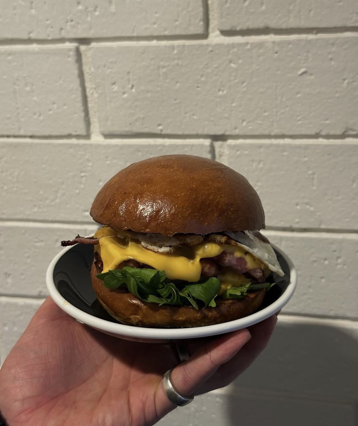 The brekky burger held up against the white brick wall