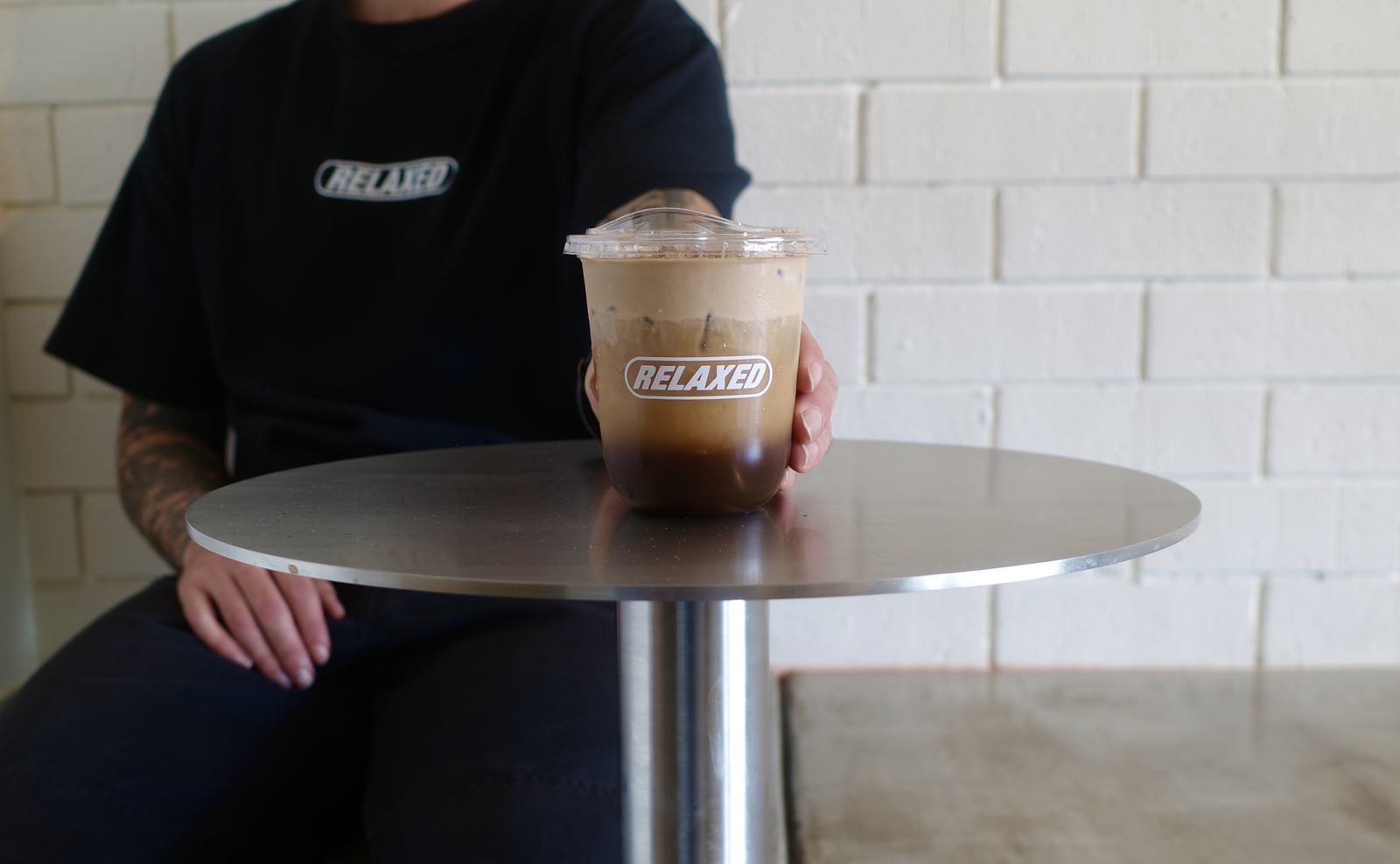 An iced coffee handed over the steel table in a Relaxed tee