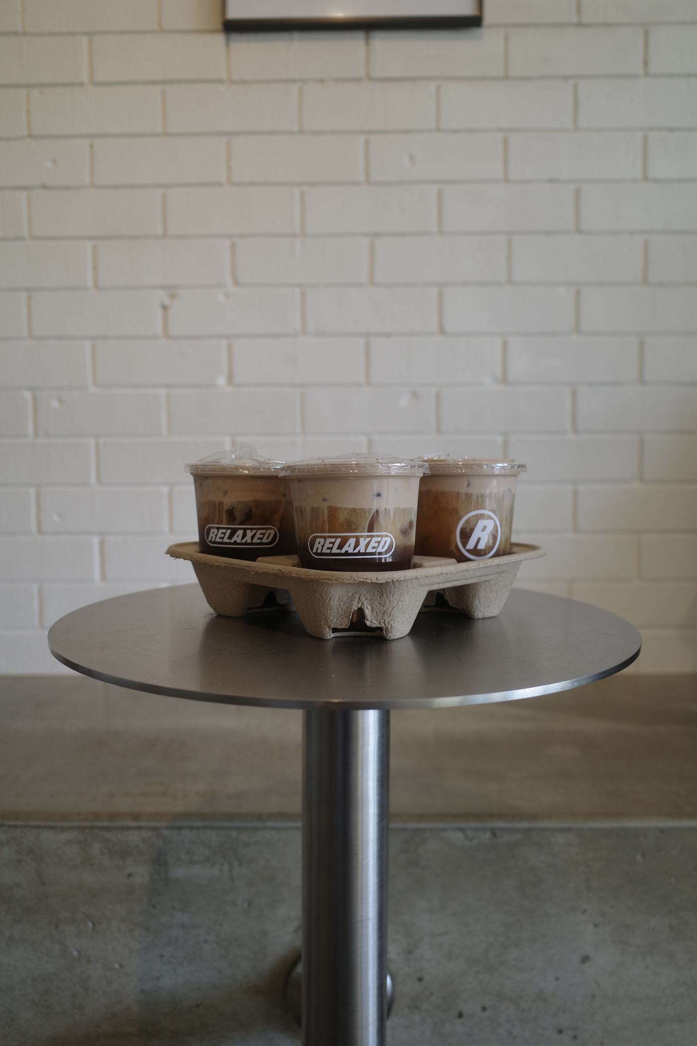 A takeaway tray of coffees on a brushed steel table against white brick